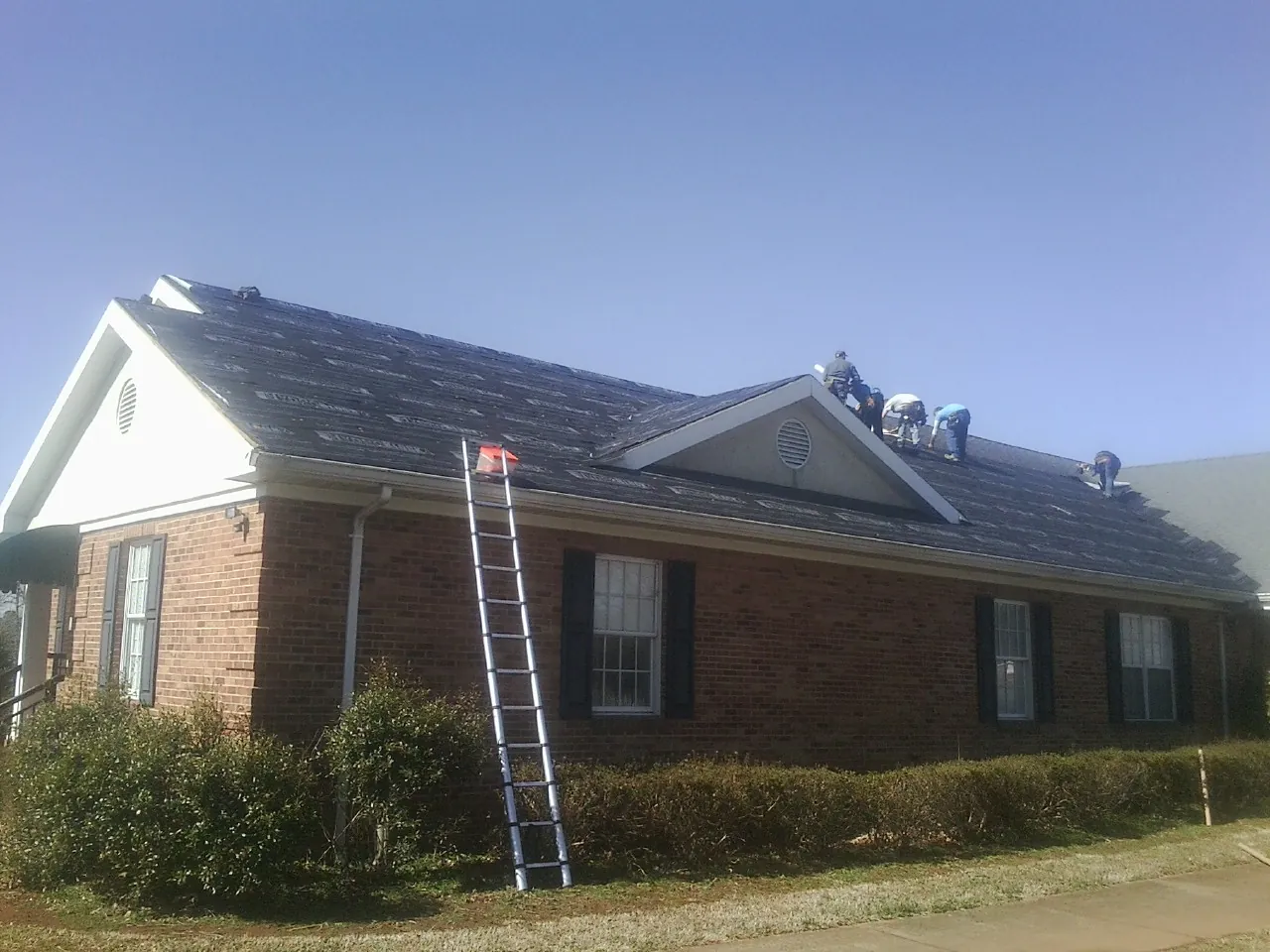 Crew tearing shingles off a brick ranch roof with a ladder set — Emergency Roof Repair work by our crew in Hamel