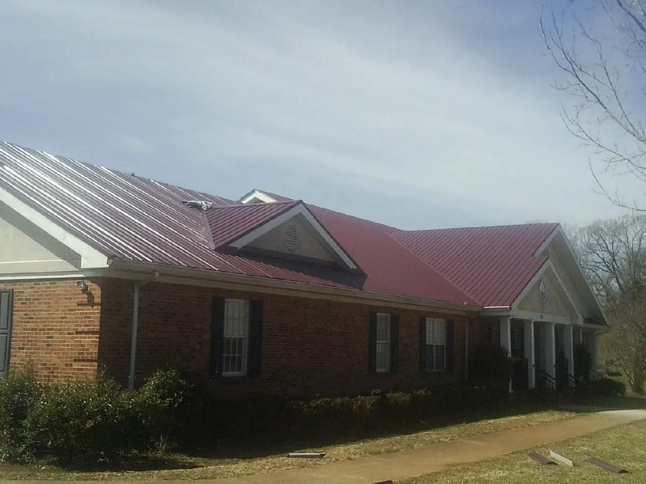 Red metal roof with gabled entries on a long brick building, from a Hail Damage Roof Repair job in Hamel