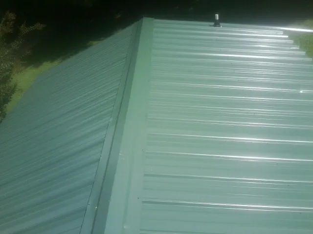 New green metal panels meeting at the ridge of a roof — Flat Roof Repair work by our crew in Hamel