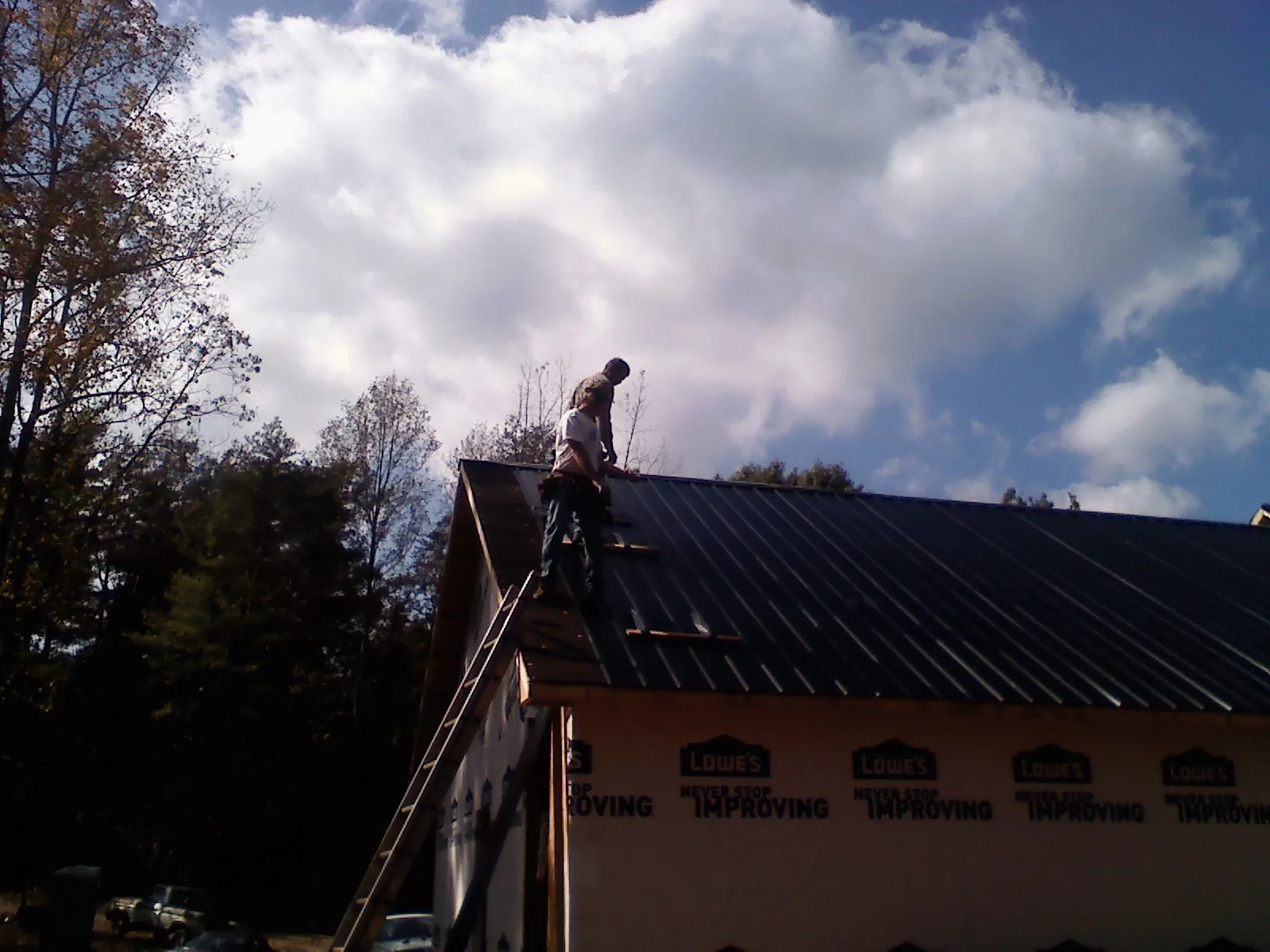 Roofer fastening dark metal panels high against a cloudy sky, from a Roof Inspection job in Hamel